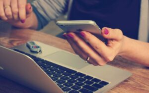 Women holding a phone in her hand while on the computer.